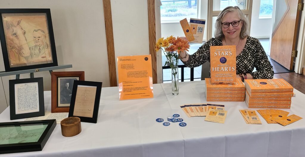 Irene seated at a book display table before her talk in Westwood MA.